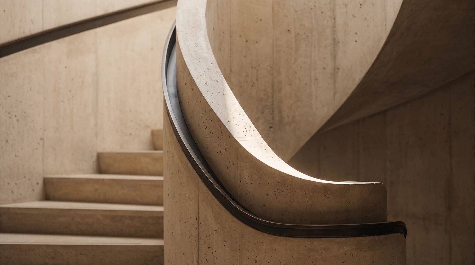 Curved concrete stair with a slim bronze handrail