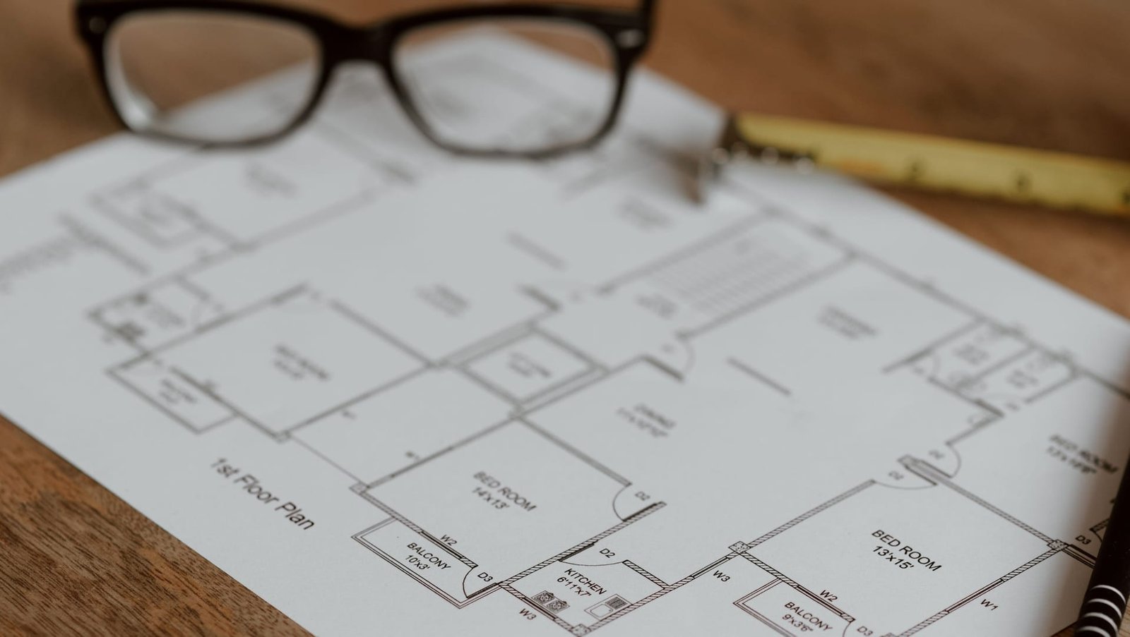 A floor plan on a timber desk with reading glasses and a pencil