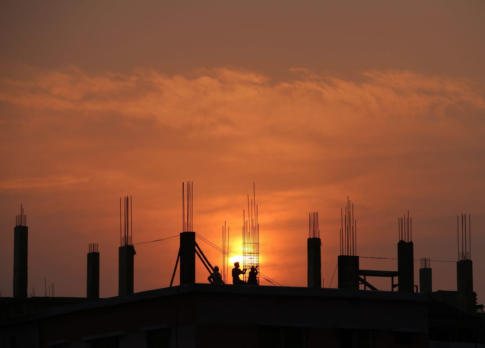 Silhouettes of a site team on a concrete frame at sunset, with reinforcement columns