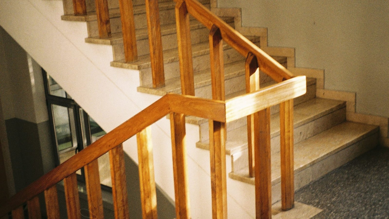 Oak-balustraded stair in low sun, with stone treads and a terrazzo floor